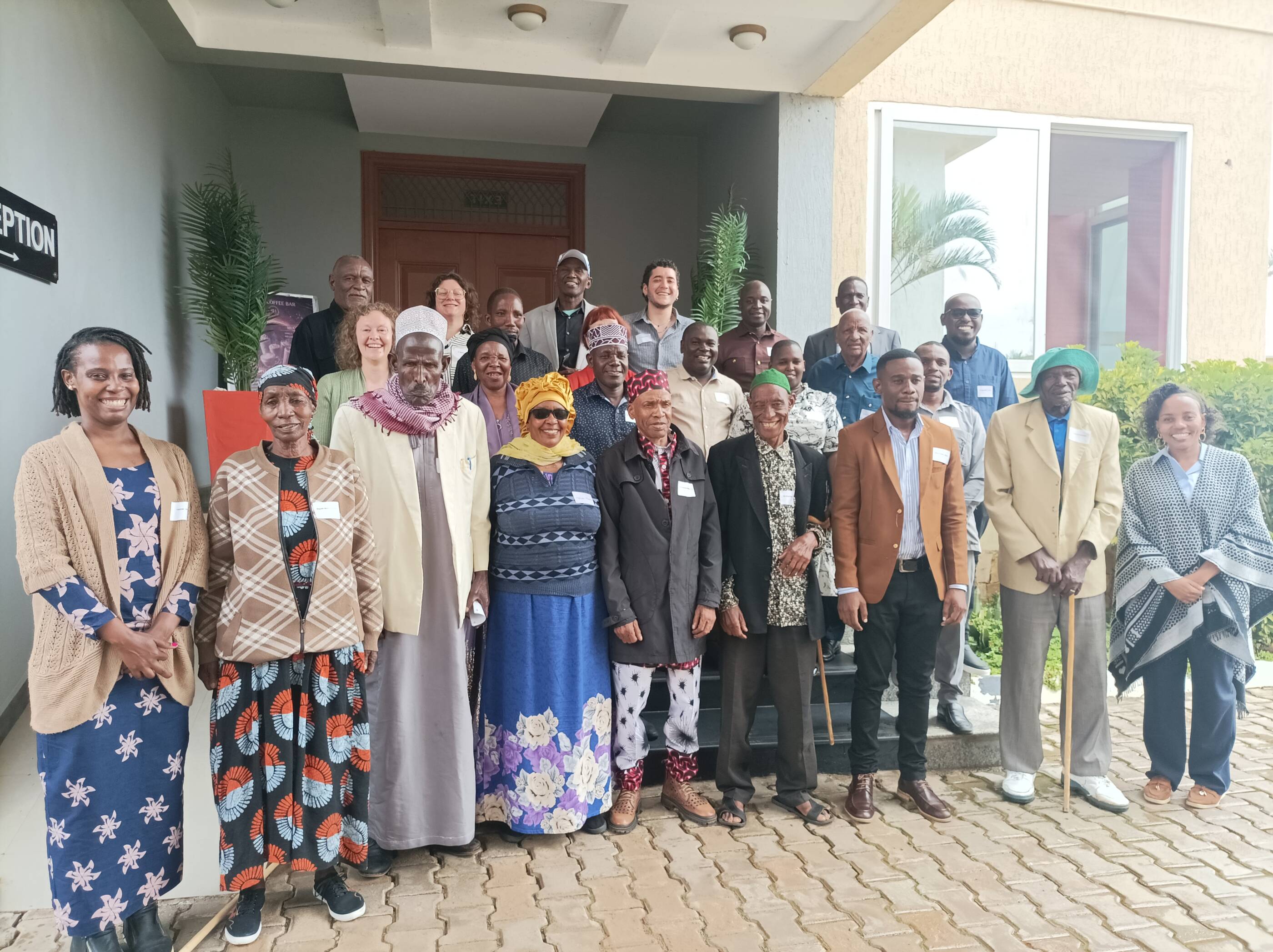 Das Foto zeigt eine Gruppe von circa 20 Personen vorwiegend schwarzer Hautfarbe, die vor einem Gebäude auf einer Treppe stehen und in die Kamera lächeln.